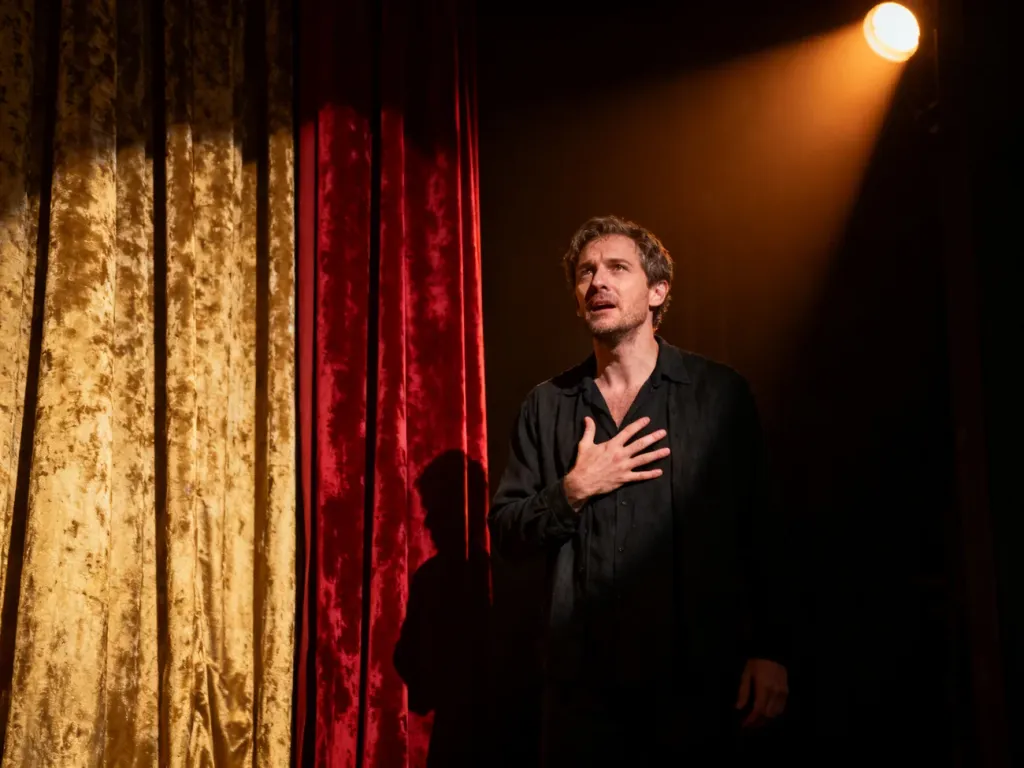 Mężczyzna w dramatycznej pozie na teatralnej scenie, ilustrujący emocjonalny i patetyczny charakter występu.